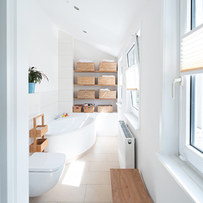Modernes, helles Badezimmer mit Eckbadewanne, Fenster und Regalen mit geflochtenen Körben.