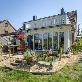 Modernes Einfamilienhaus mit Wintergarten, Terrasse und gepflegtem Garten bei Sonnenschein.