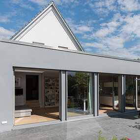 Modernes Einfamilienhaus mit großer Terrasse, bodentiefen Fenstern und Flachdachanbau.