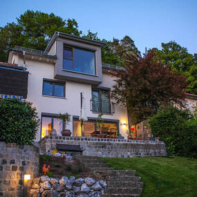 Modernes Einfamilienhaus mit großer Terrasse und Garten am Waldrand bei Abenddämmerung.