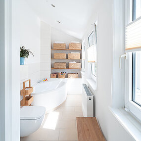 Helles modernes Badezimmer mit Badewanne, Fenster, Toilette und Regalen mit Körben.