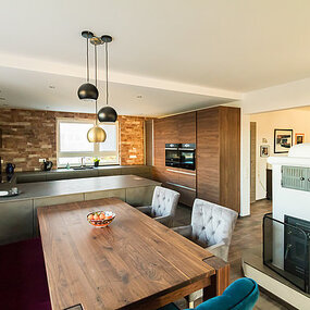 Moderne offene Küche mit Holztisch, Designlampen und gemauertem Kamin im Essbereich.